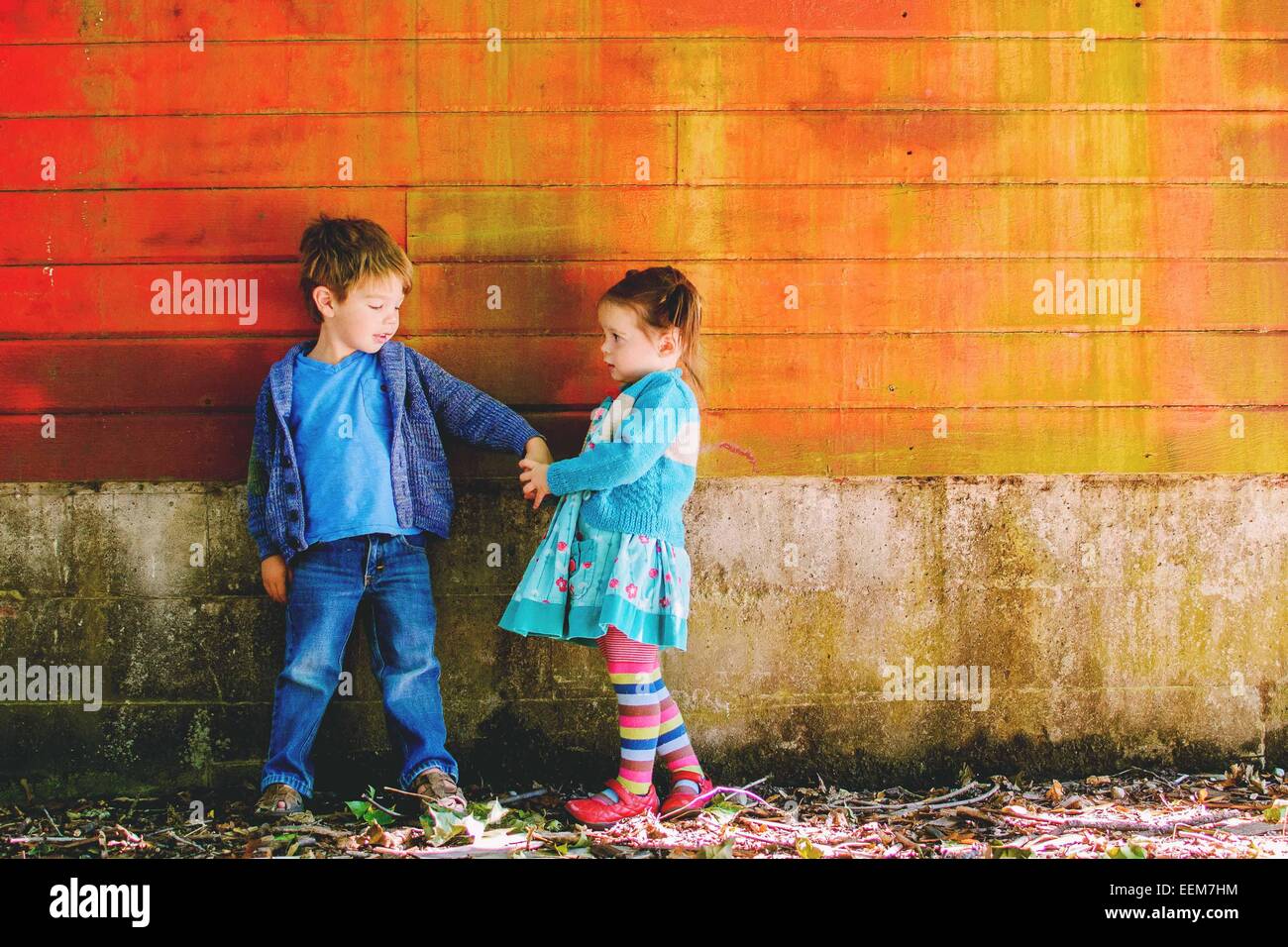 Boy and girl standing by a wall holding hands Stock Photo