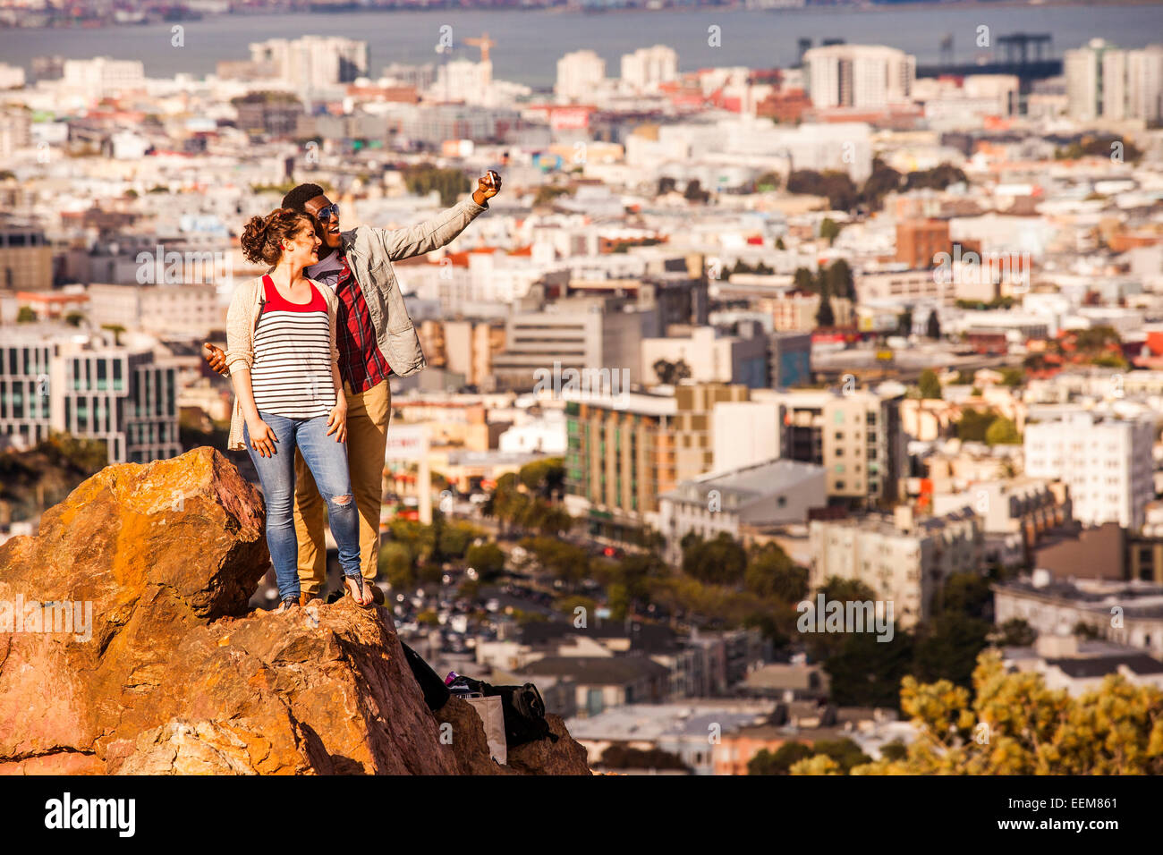 Couple taking cell phone selfie on rock overlooking scenic view of cityscape Stock Photo