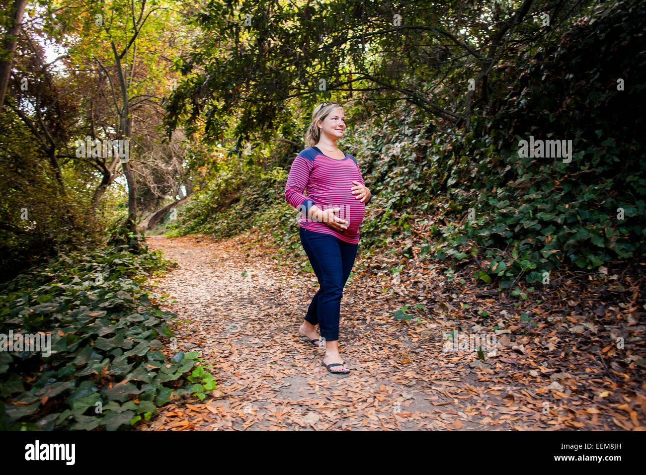 Pregnant Caucasian woman holding her stomach on forest path Stock Photo ...