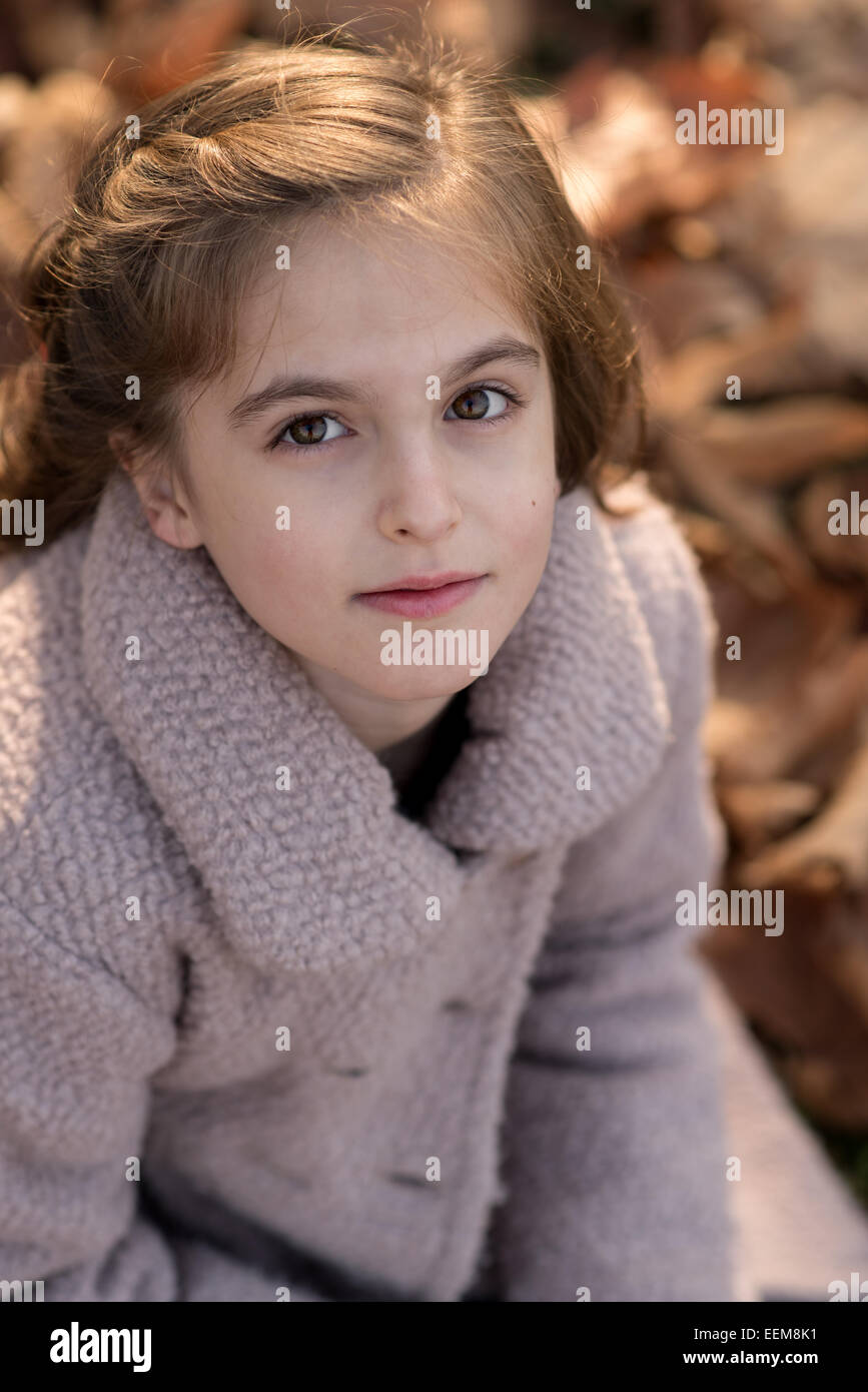 Cute girl (8-9) sitting in autumn leaves Stock Photo