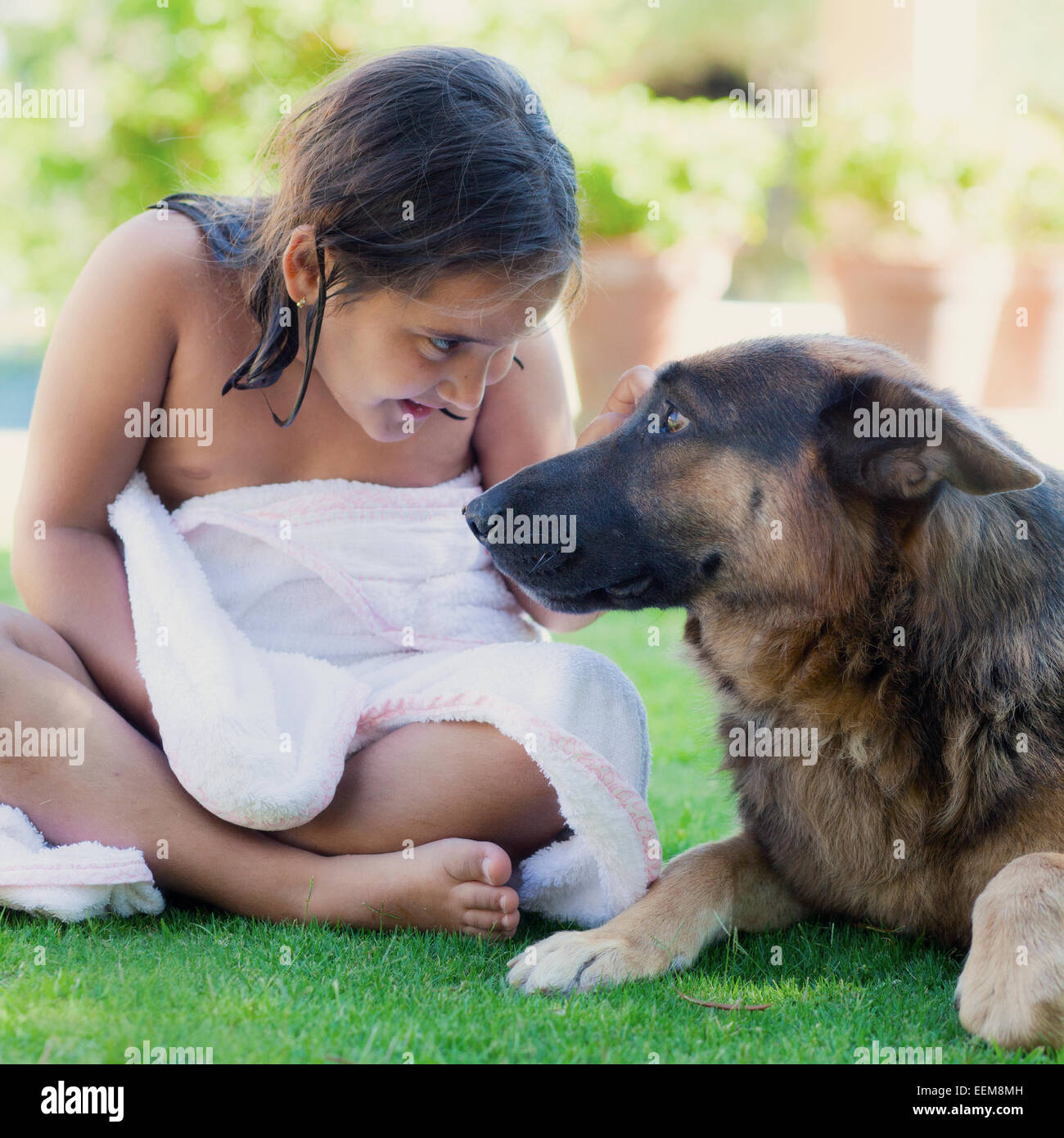 Girl wrapped in a towel sitting on grass next to her dog Stock Photo