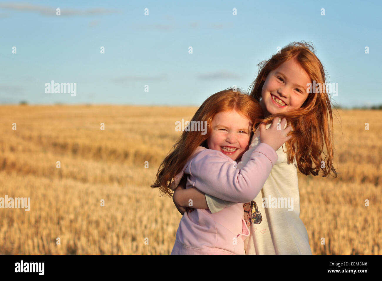 Sisters (4-5, 6-7) hugging in field Stock Photo