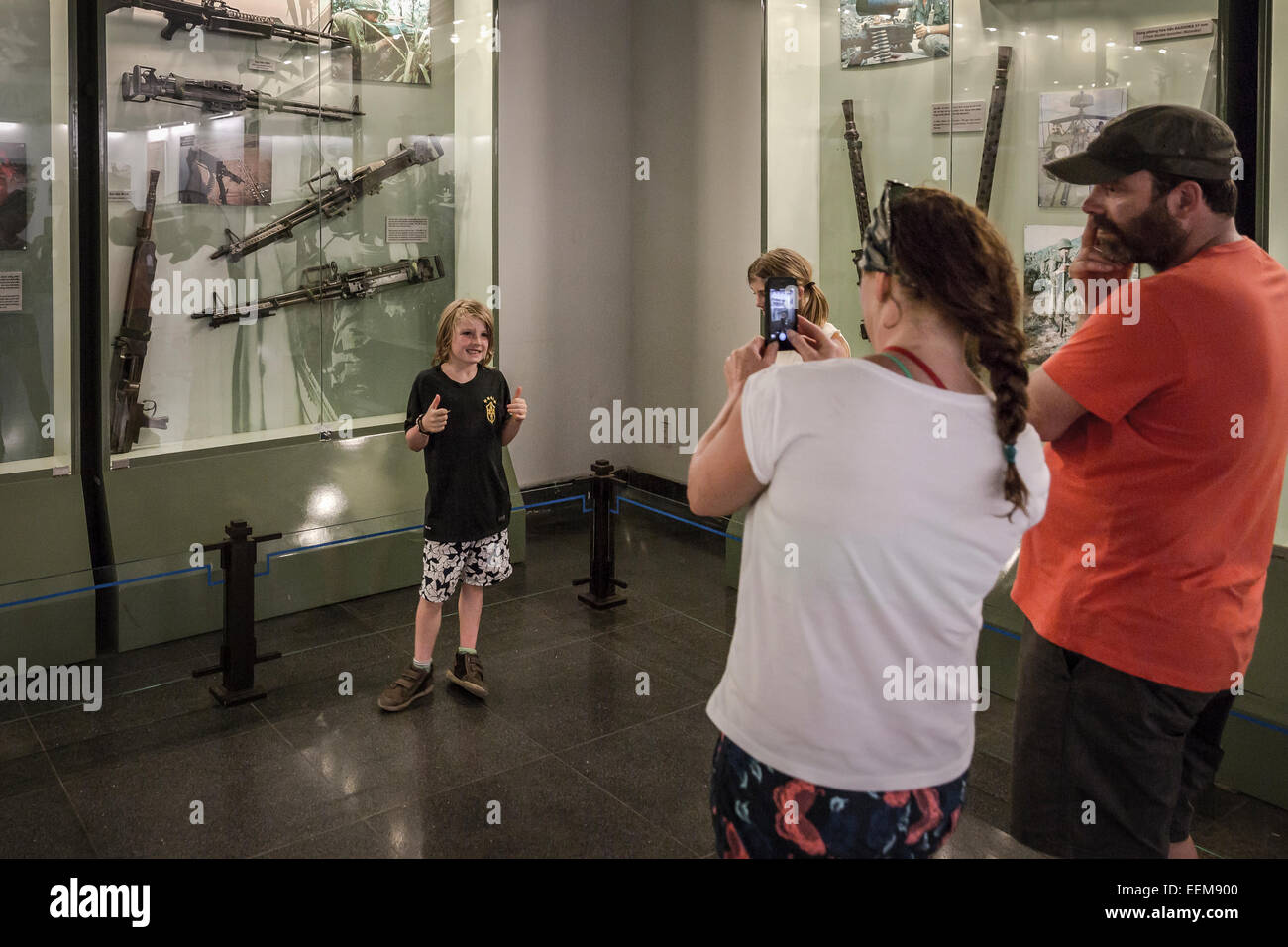 Museum Memories of War. A woman photographs her son in front of one of the windows that expose weapons used by the US army. Stock Photo