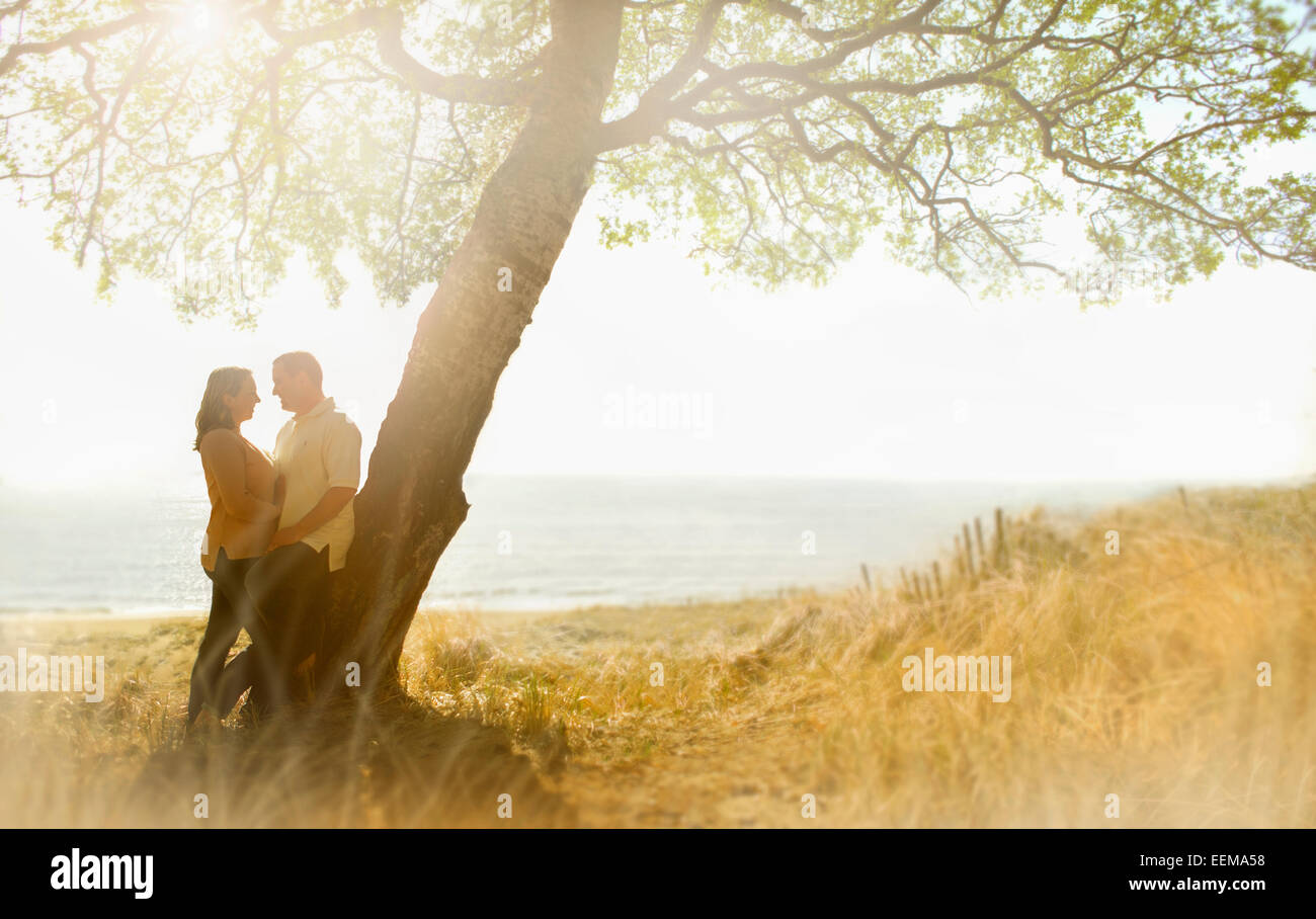 Caucasian couple hugging near tree in field Stock Photo