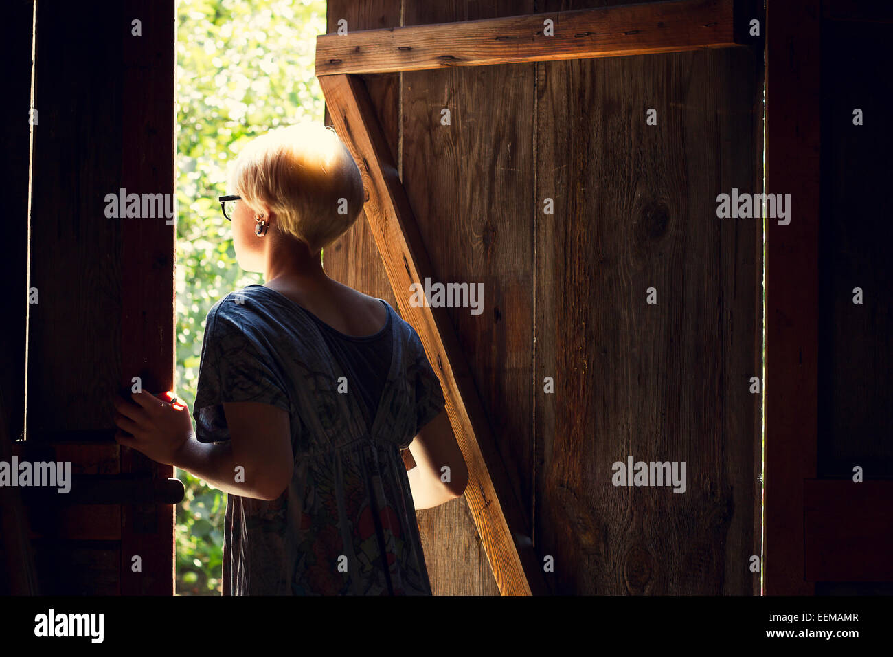 Caucasian woman looking out barn door Stock Photo