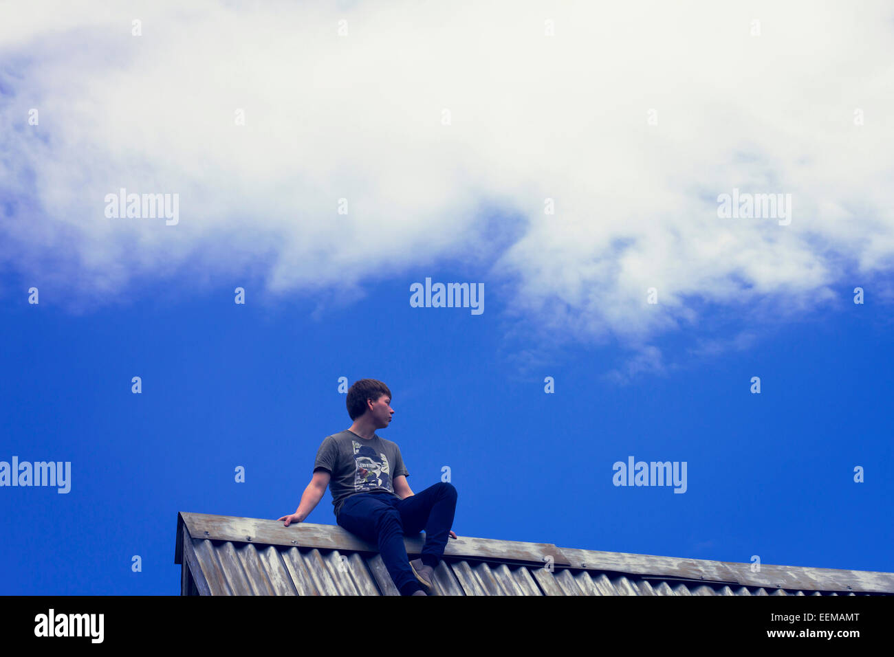 Low angle view of Caucasian boy sitting on tin roof Stock Photo