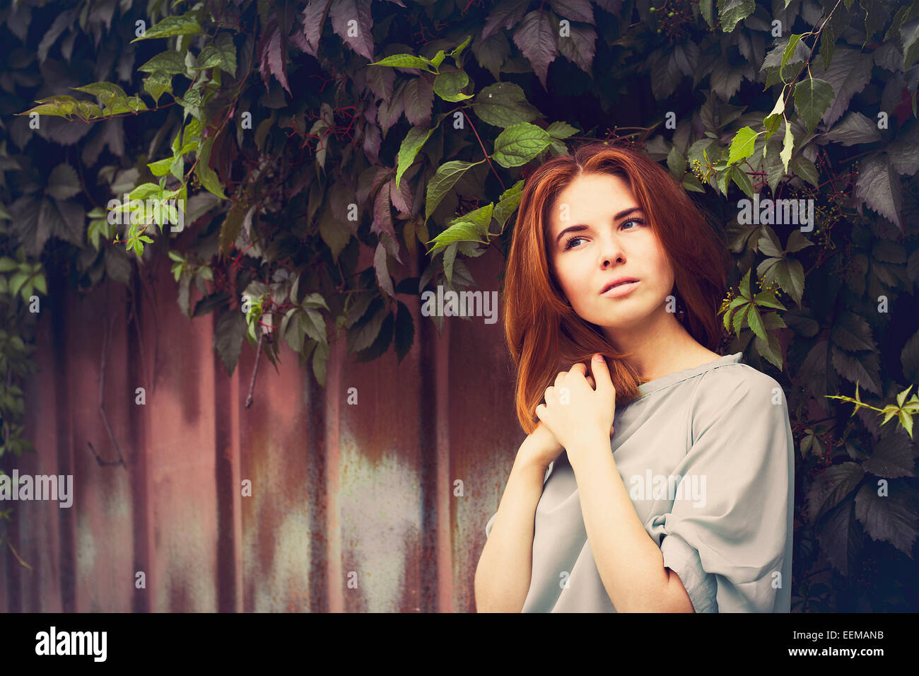 Caucasian woman standing under leaves by fence Stock Photo