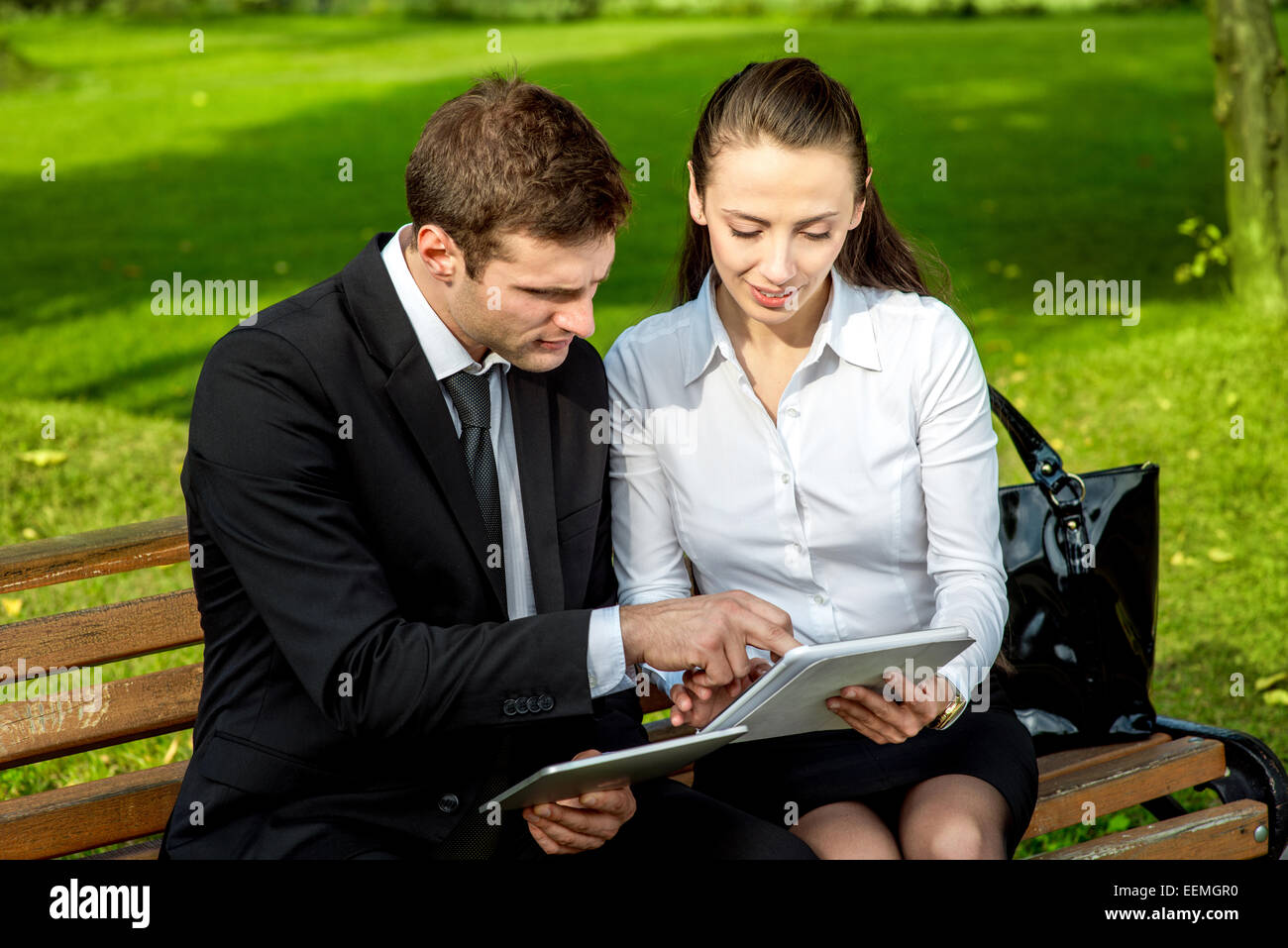 Young Business couple sitting on the bench and reading or working with tablets outdoors. Stock Photo