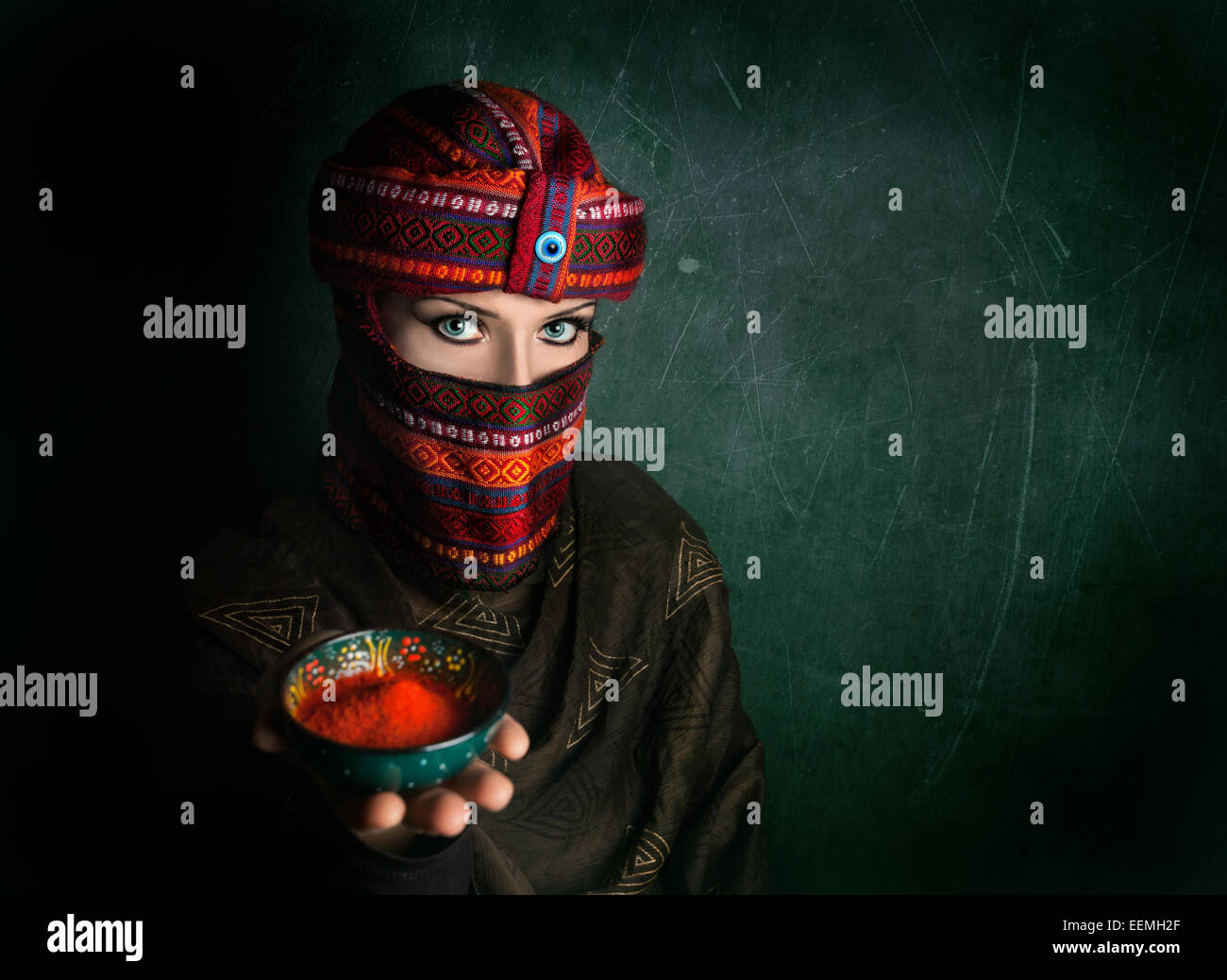 Oriental woman in turban offering red chili powder at green textured wall Stock Photo