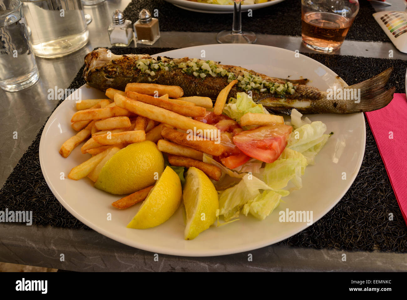 Grilled sea bass with french fries and lemon slices on a plate, France