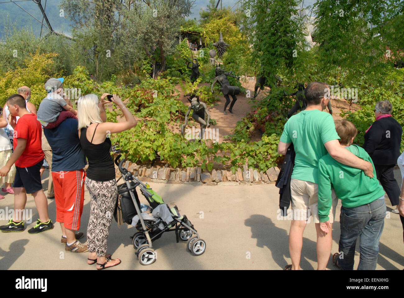 Eden Project, Cornwall, UK.  Visitors in front of sculpted figures representing the Rites of Dionysus.  Mediterranean Biome. Stock Photo