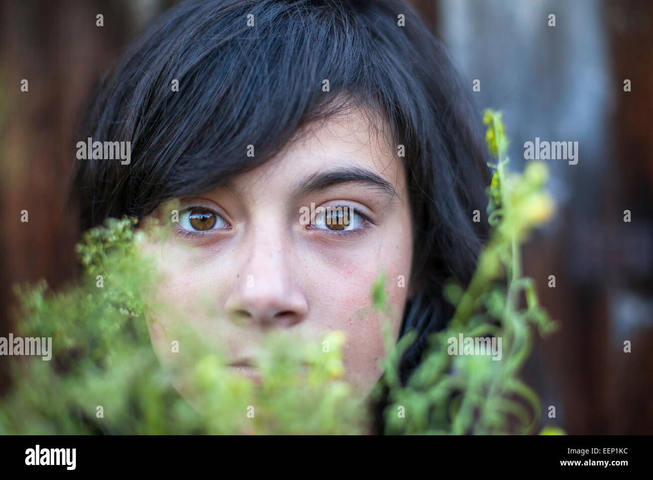 Closeup of black-haired teen girl with expressive eyes, hidden in the greenery of the garden. Emo. Stock Photo