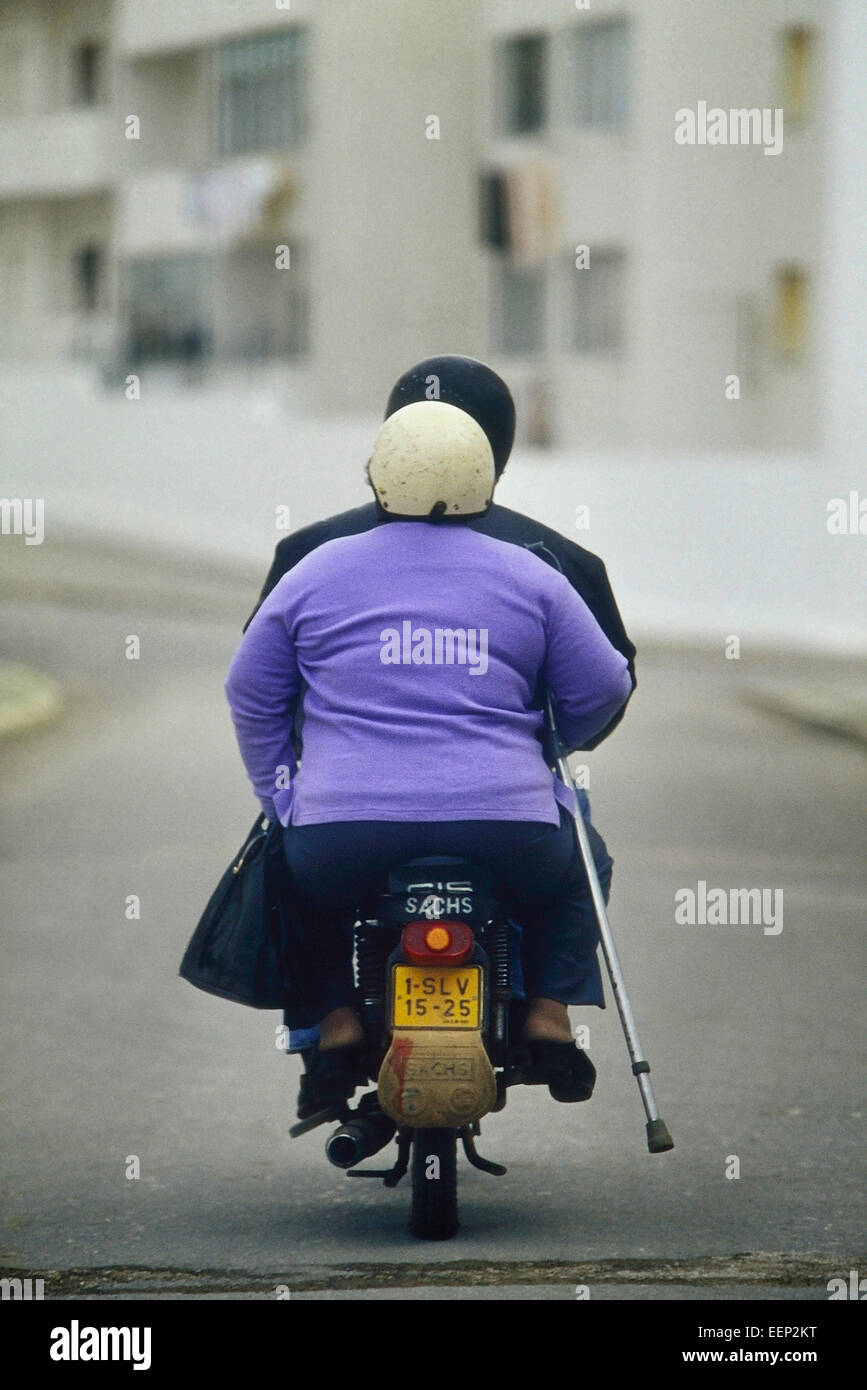 A disabled woman with a crutch riding on the back of a motor scooter. Portugal. Stock Photo