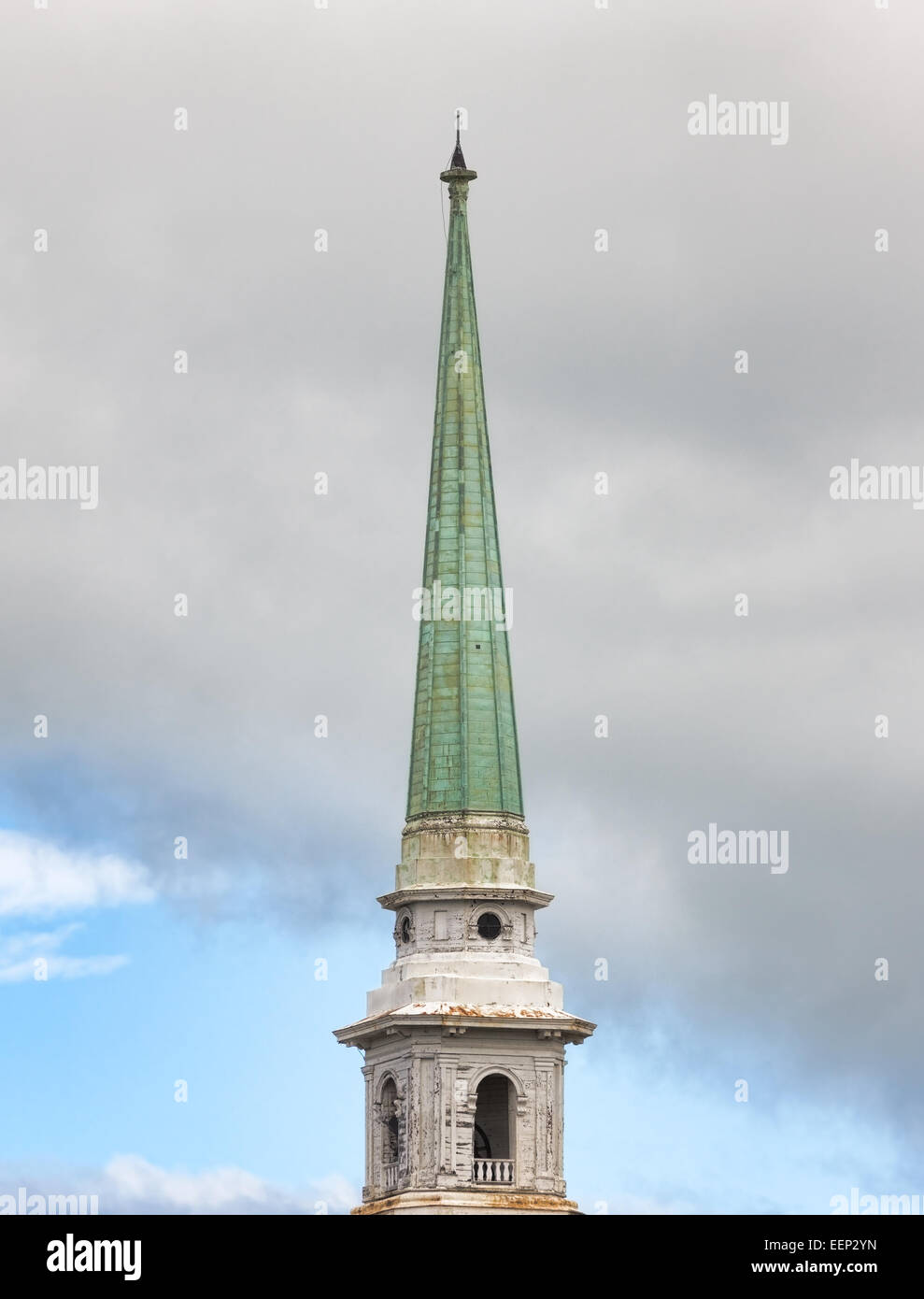 An old metal covered church spire in the foreground with clouds and sky in the background. Stock Photo