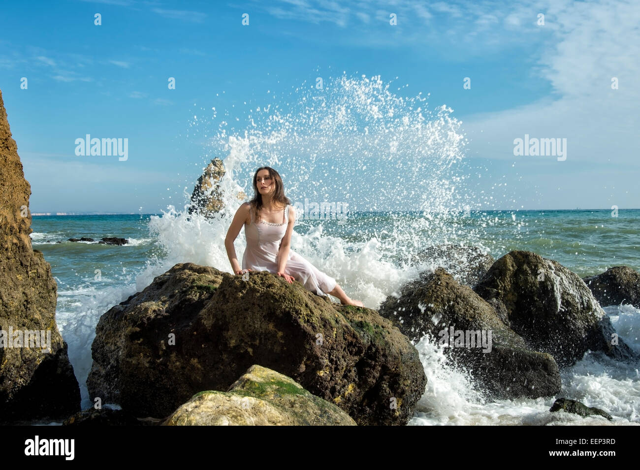 woman lying posing on a rock with crashing waves Stock Photo
