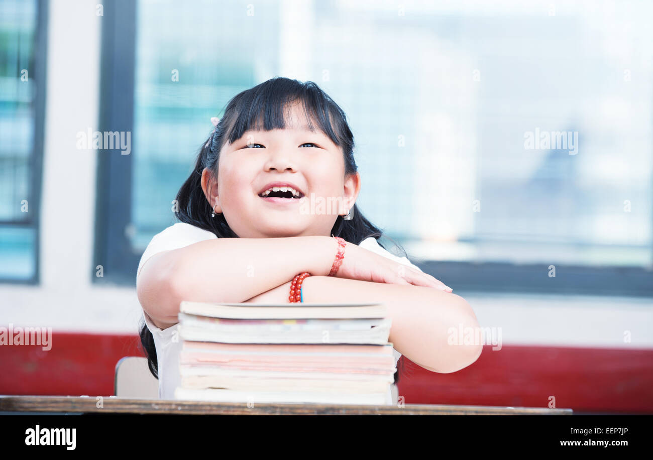 Portrait of cute asian girl on top of book stack looking upwards. School classroom happy scene. Stock Photo