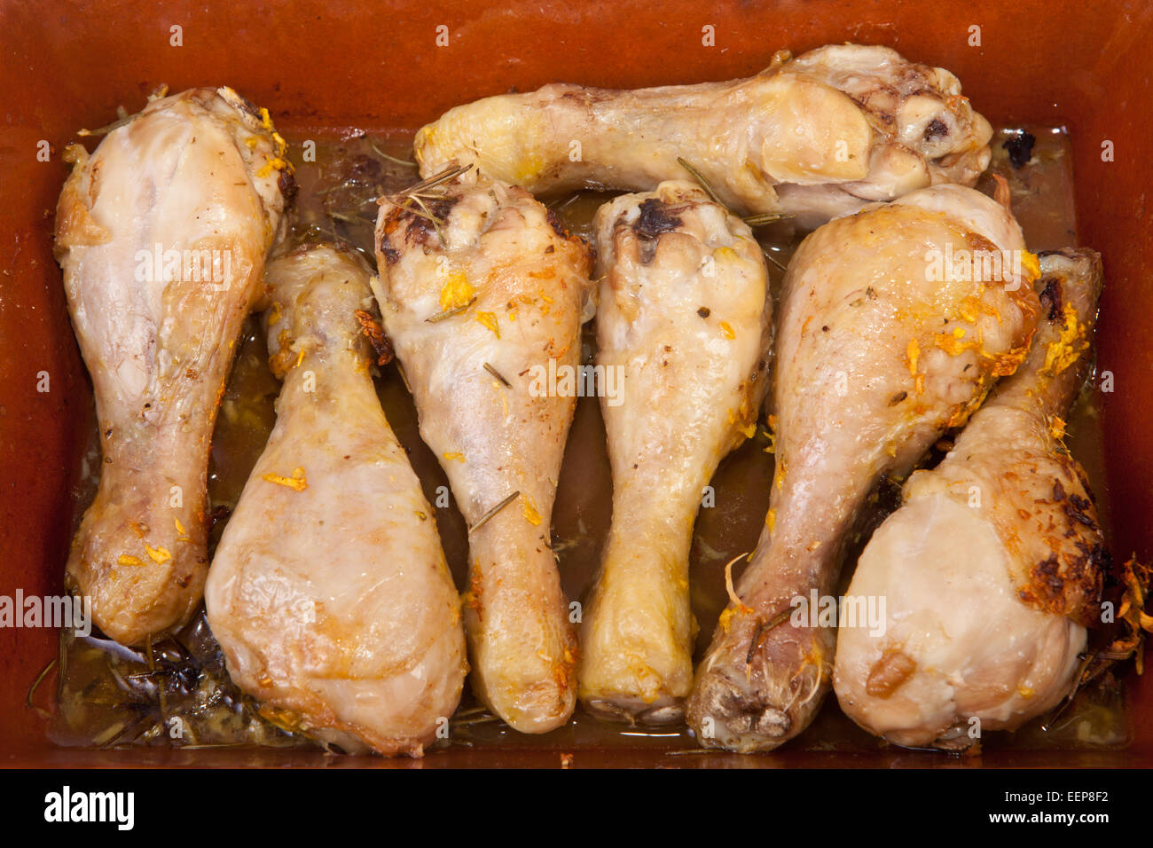 Oven-cooked chicken legs with herbs on a glazed clay pan Stock Photo