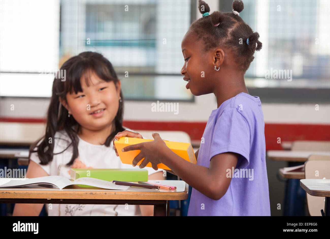 Two young multiracial african asian girls smiling at classroom desk. Stock Photo