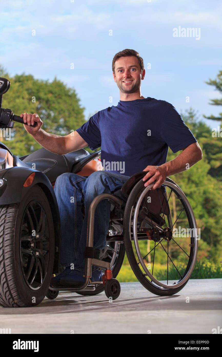 Man with spinal cord injury sitting in wheelchair beside his custom motorcycle Stock Photo