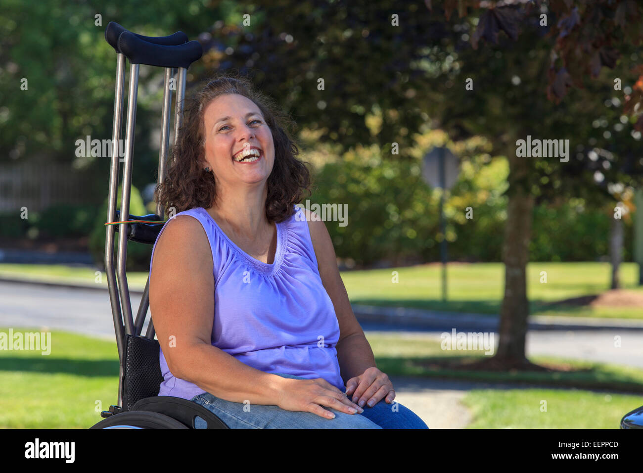 Woman with Spina Bifida laughing while sitting in wheelchair with crutches Stock Photo