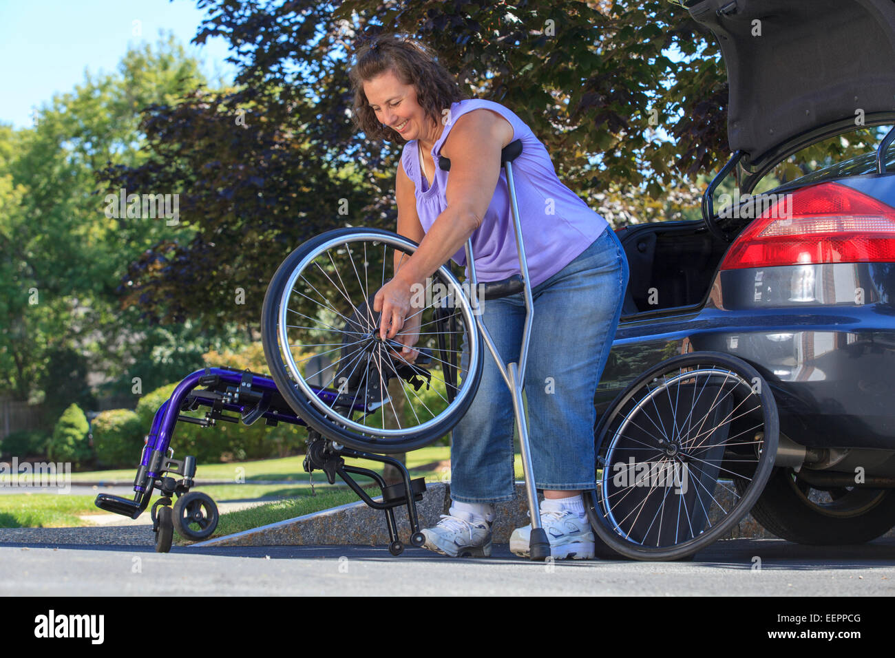 Woman with Spina Bifida using crutches to take wheelchair apart for traveling in the car Stock Photo