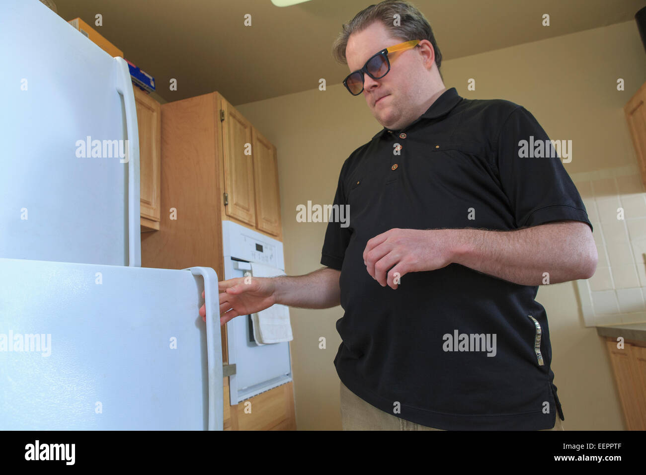 Man with congenital blindness using the refrigerator in his kitchen