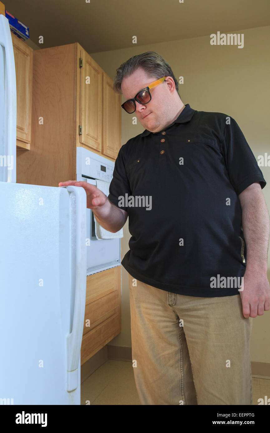 Man with congenital blindness using the refrigerator in his kitchen Stock Photo