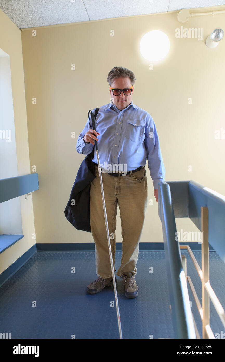 Man with congenital blindness using his cane in an apartment hallway Stock Photo