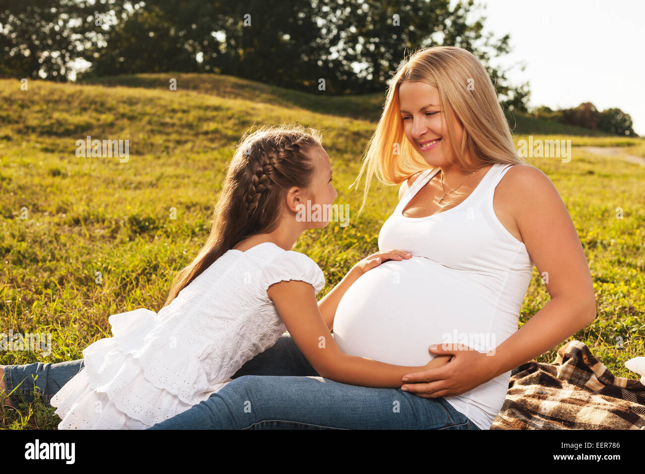 Cute little girl hugging her mother's pregnant belly. Happy sister to be is excited about meeting new baby. Mother's day concept Stock Photo