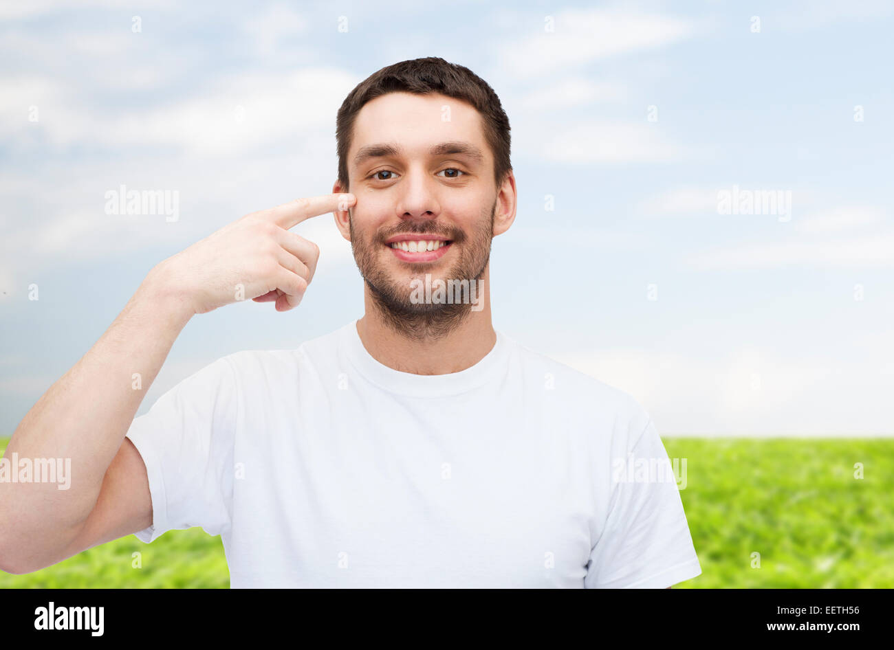 smiling young handsome man pointing to eyes Stock Photo