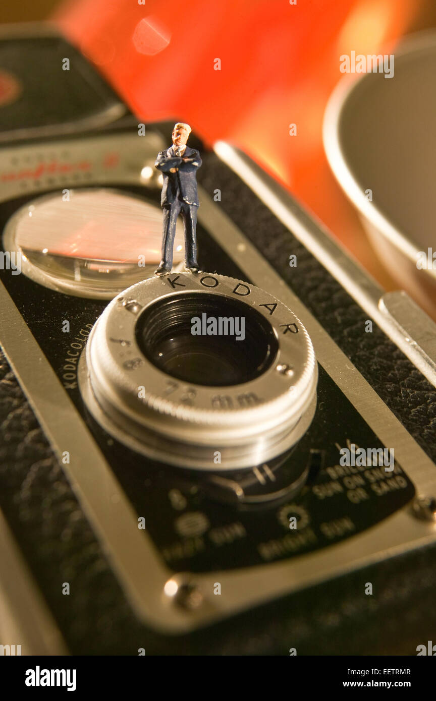 Conceptual macro image of figurine Businessman standing on the lens of a vintage camera. Stock Photo