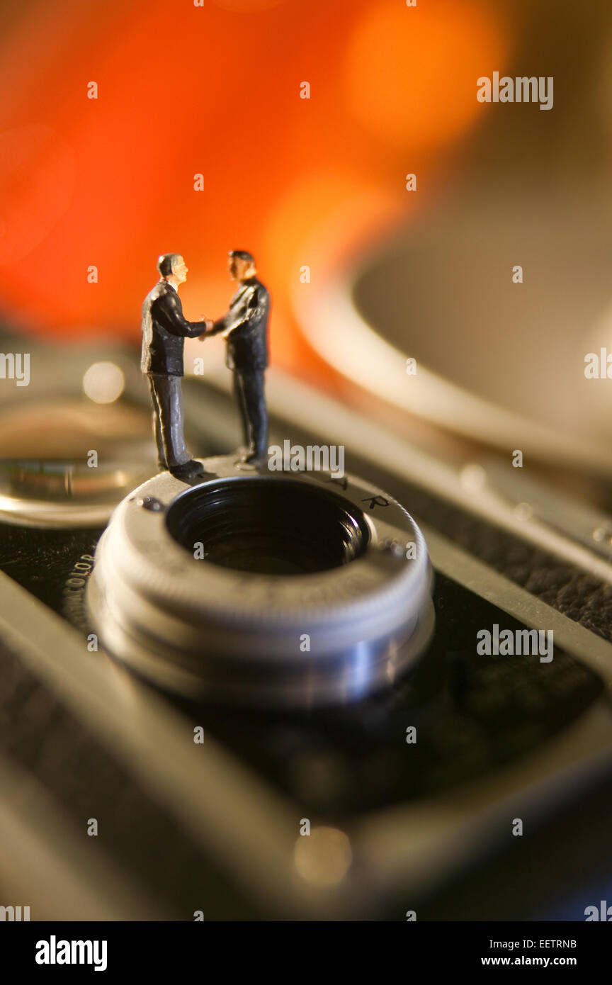 Conceptual macro image of figurine Businessmen shaking hands on a vintage camera. Stock Photo