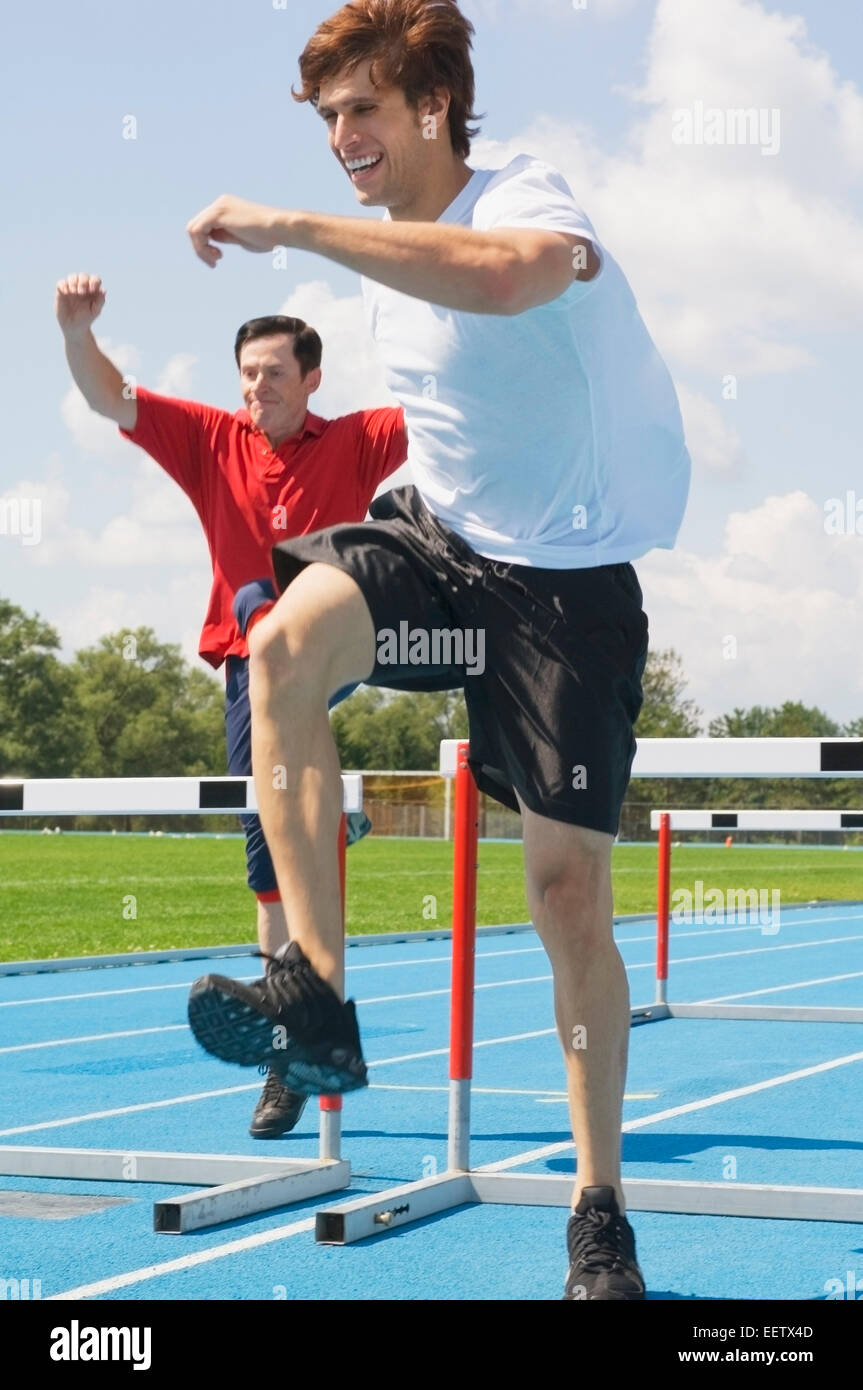 Two men jumping hurdles on a track Stock Photo Alamy