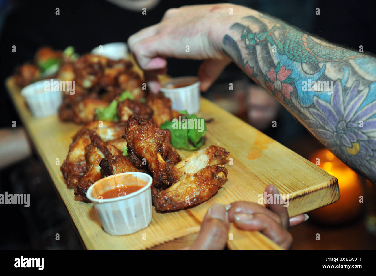 Chicken is served on a wooden platter to a guest with a completely tattooed arm. Stock Photo