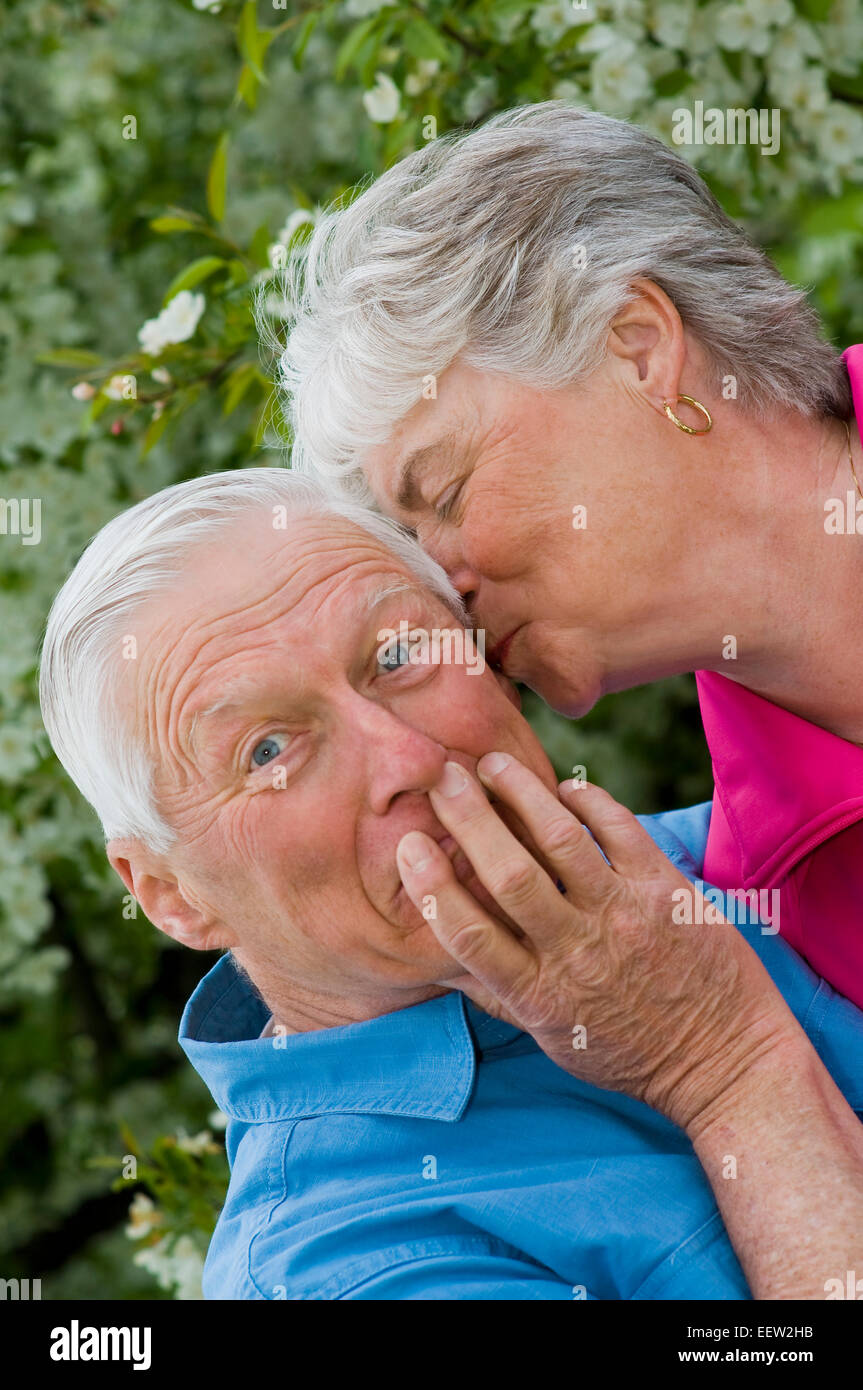 Senior woman whispering into ear of husband Stock Photo