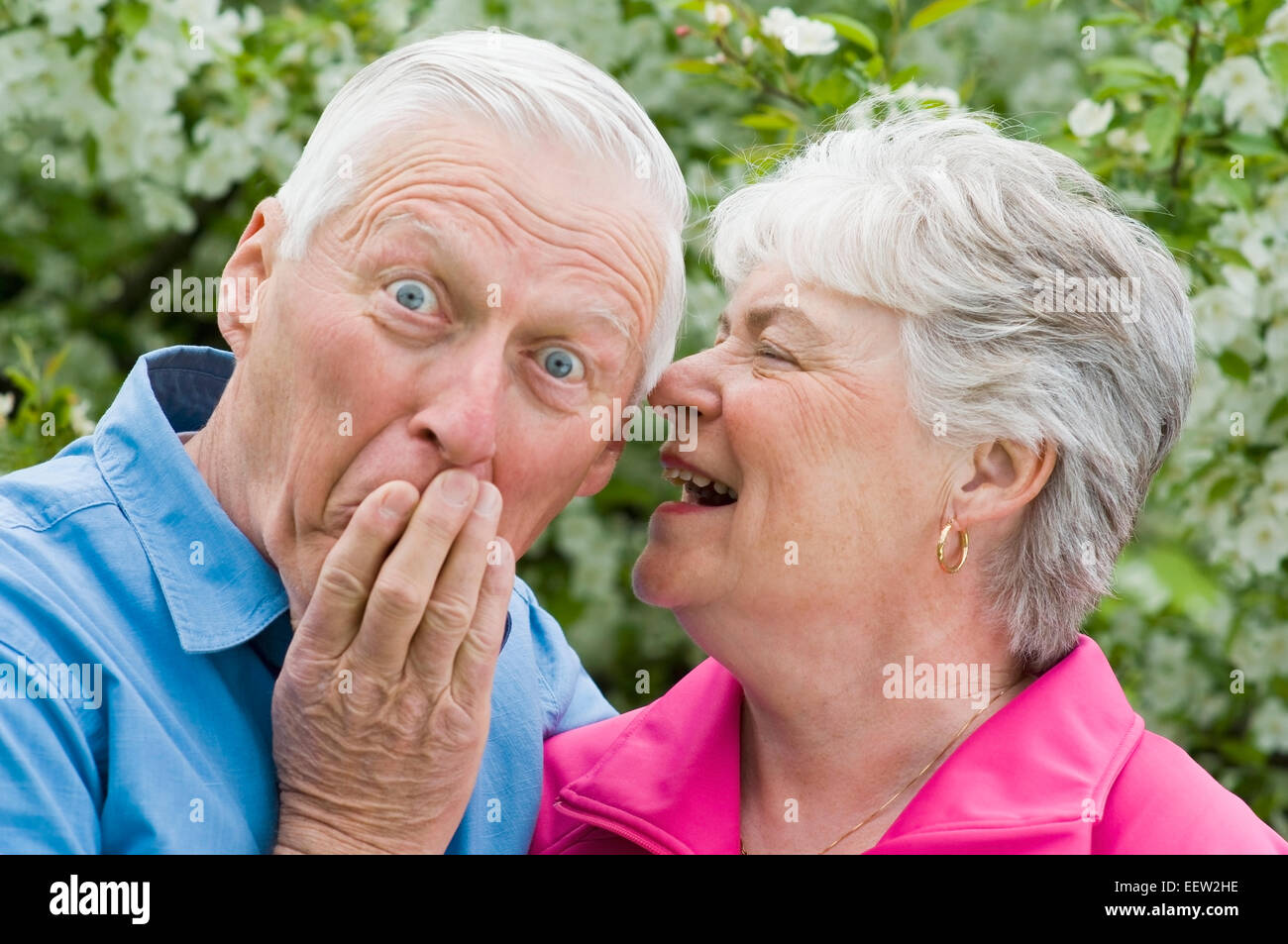 Senior woman whispering into ear of husband Stock Photo