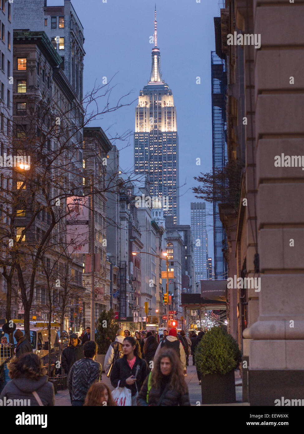 Fifth Avenue with the floodlit Empire State Building in the back. Shoppers crowd the sidewalk while the lights start coming on Stock Photo