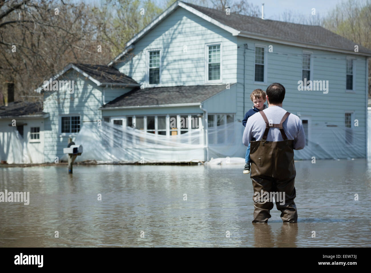 Father holding son and looking at floodwaters surrounding house Stock Photo