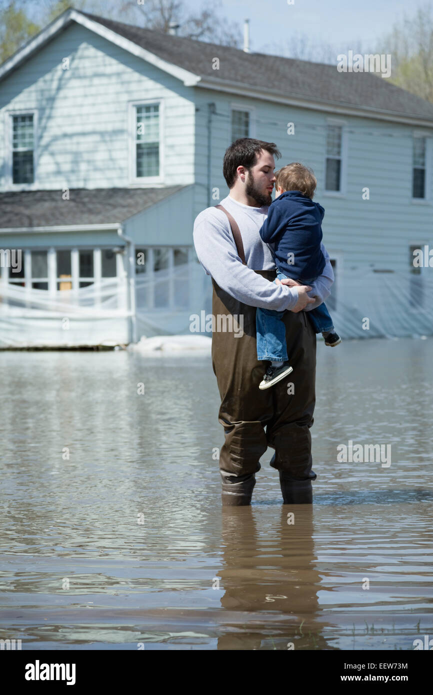 Man with son standing in front of house surrounded by floodwaters Stock Photo