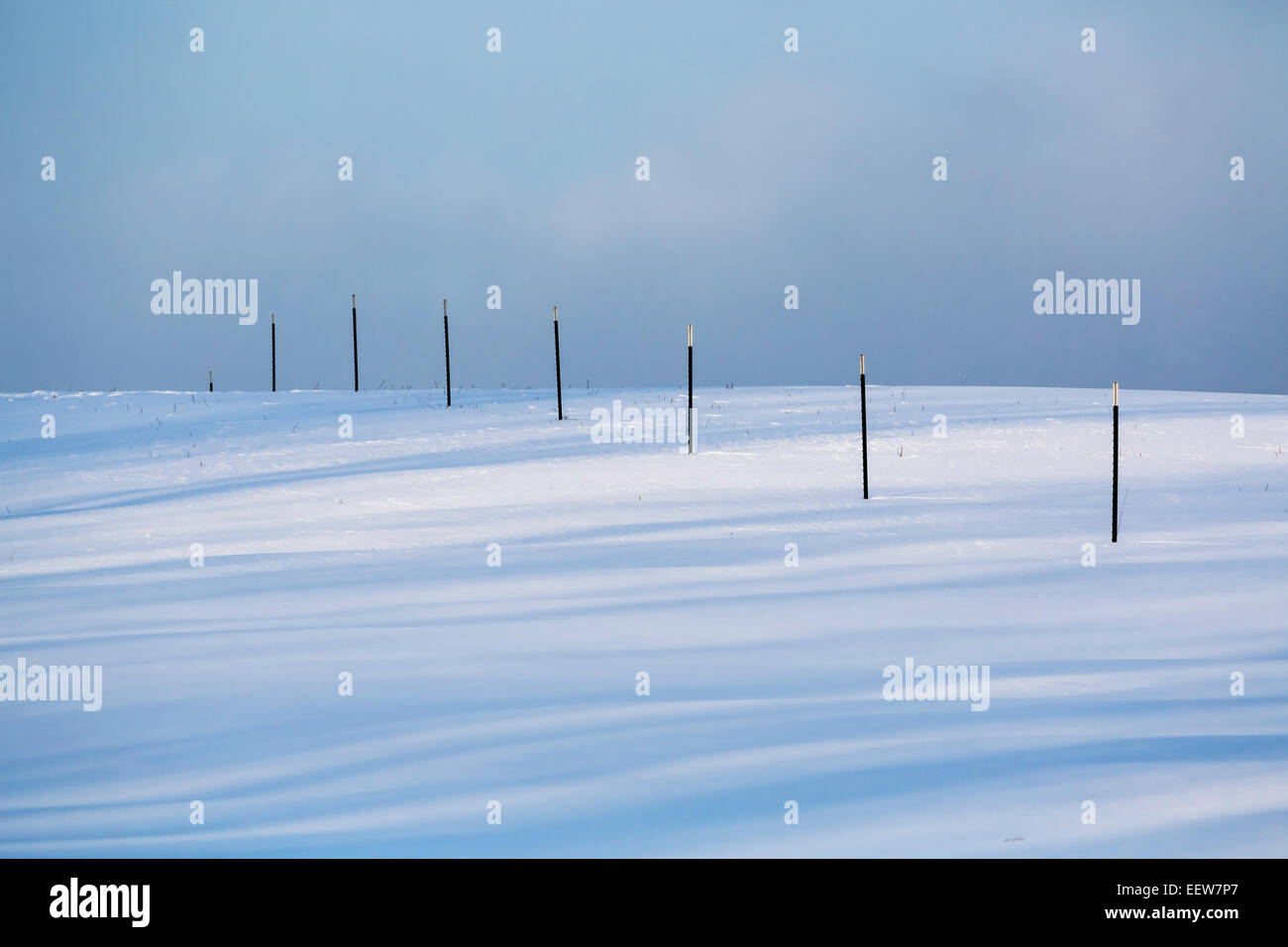 Fence with long shadows crossing a snowy farm field in Mecosta County near Big Rapids and Stanwood, Michigan, USA Stock Photo