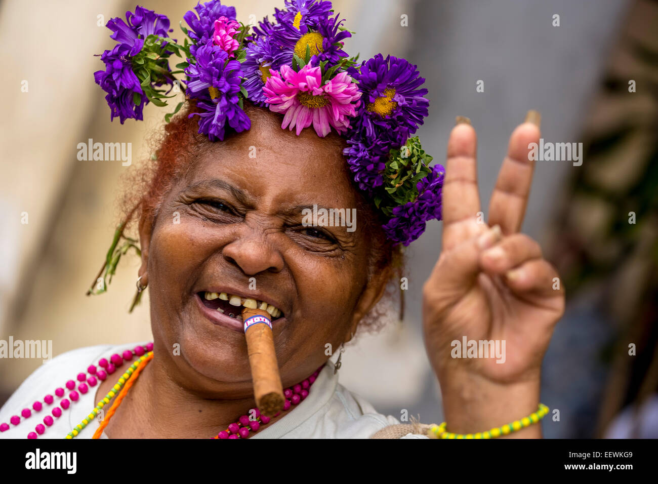 Elderly Cuban woman with flower headdress and cigar, making peace sign, Havana, Cuba Stock Photo