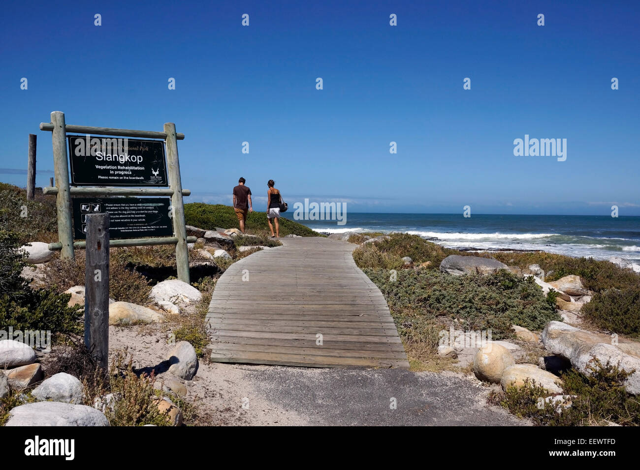 Couple walking along the walkway in the Table Mountain National Park towards the Slangkop Point lighthouse in Kommetjie. Stock Photo