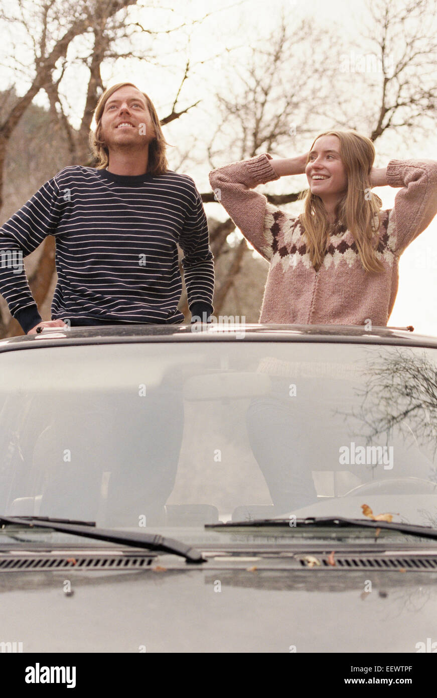 Young couple standing in their car, looking through sunroof. Stock Photo