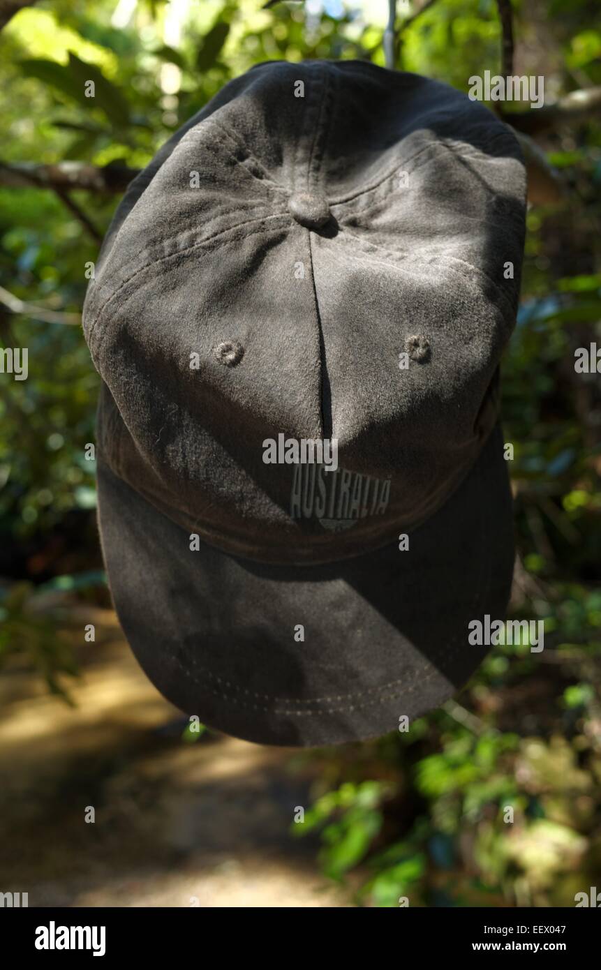 An Australia cap hanging from a tree branch on a padded clothes hanger near a waterfall Stock