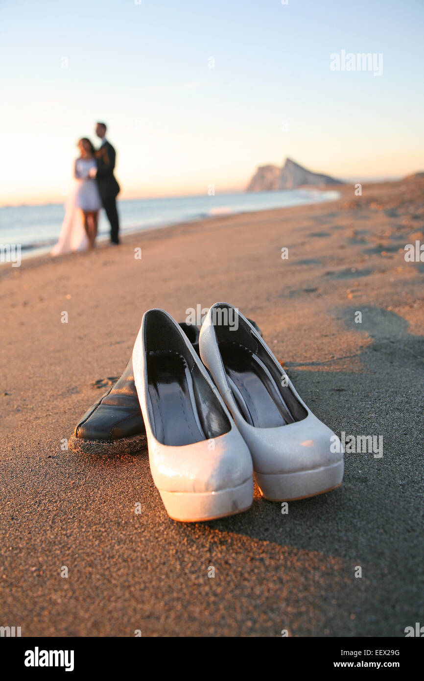 Bride and groom in beach shore in Cadiz, Spain at sunrise with rock of Gibraltar in background and wedding shoes in foreground. Stock Photo