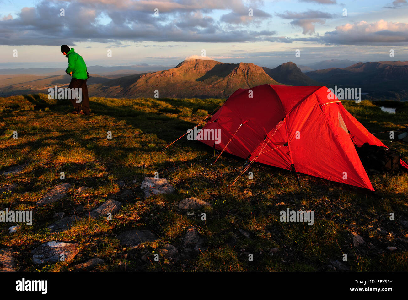 A hiker passing by a tent at the top of the Suilven Mountain in Scotland, United Kingdom. Stock Photo