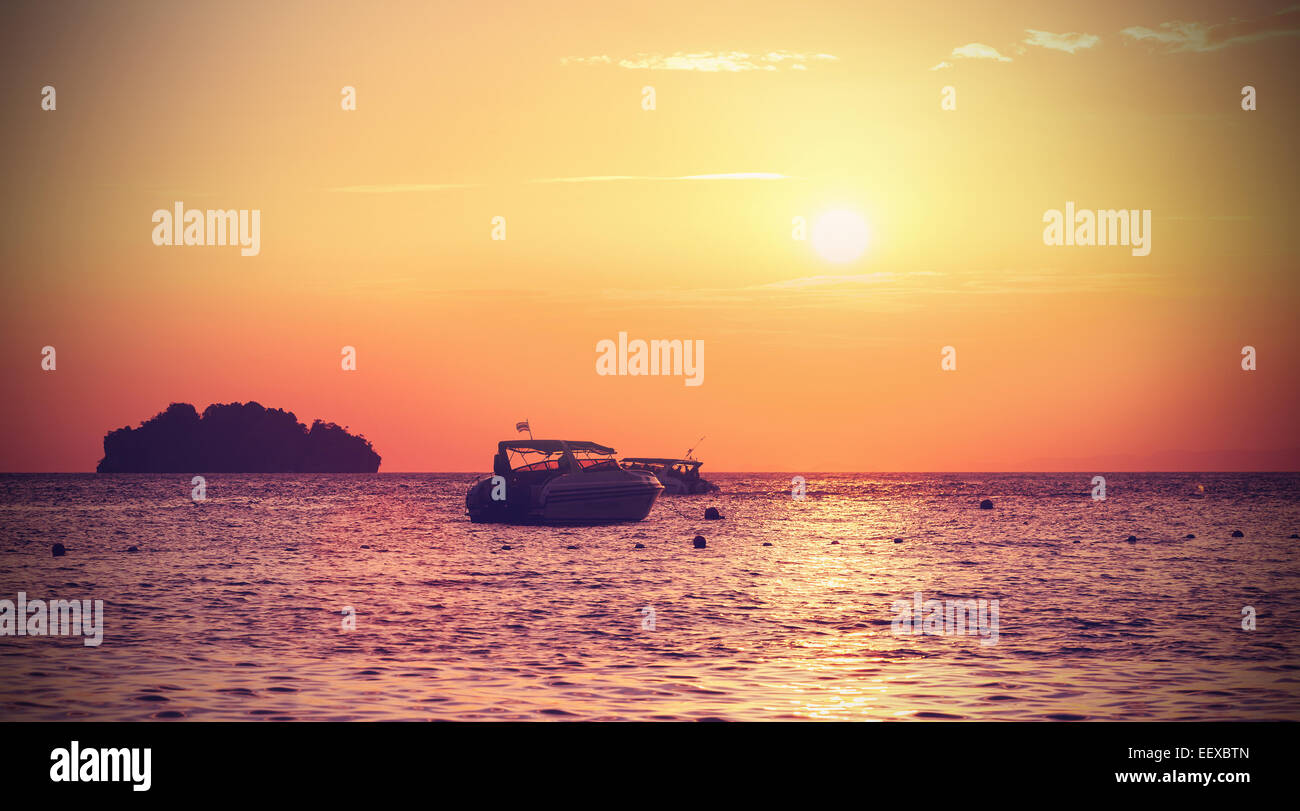 Vintage filtered silhouette of a little island and small boat at sunset. Stock Photo