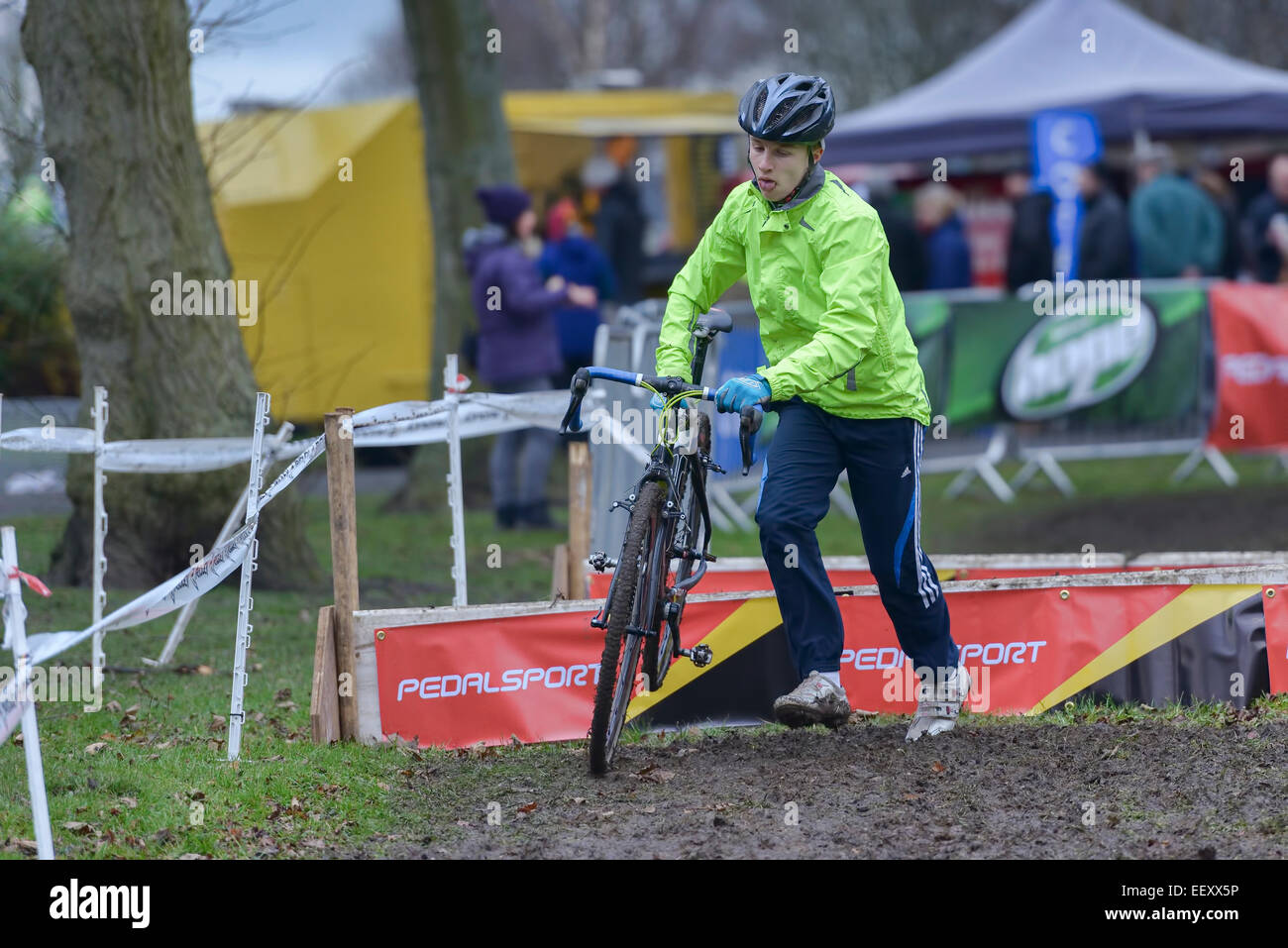 A male competitor clears a barrier hurdle, carrying his bike bicycle during a cyclocross 'cyclo cross' race Stock Photo