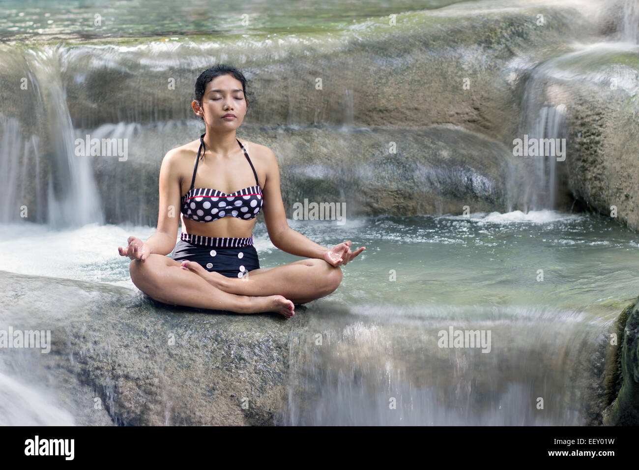 woman in retro swimsuit doing yoga in a waterfall Stock Photo