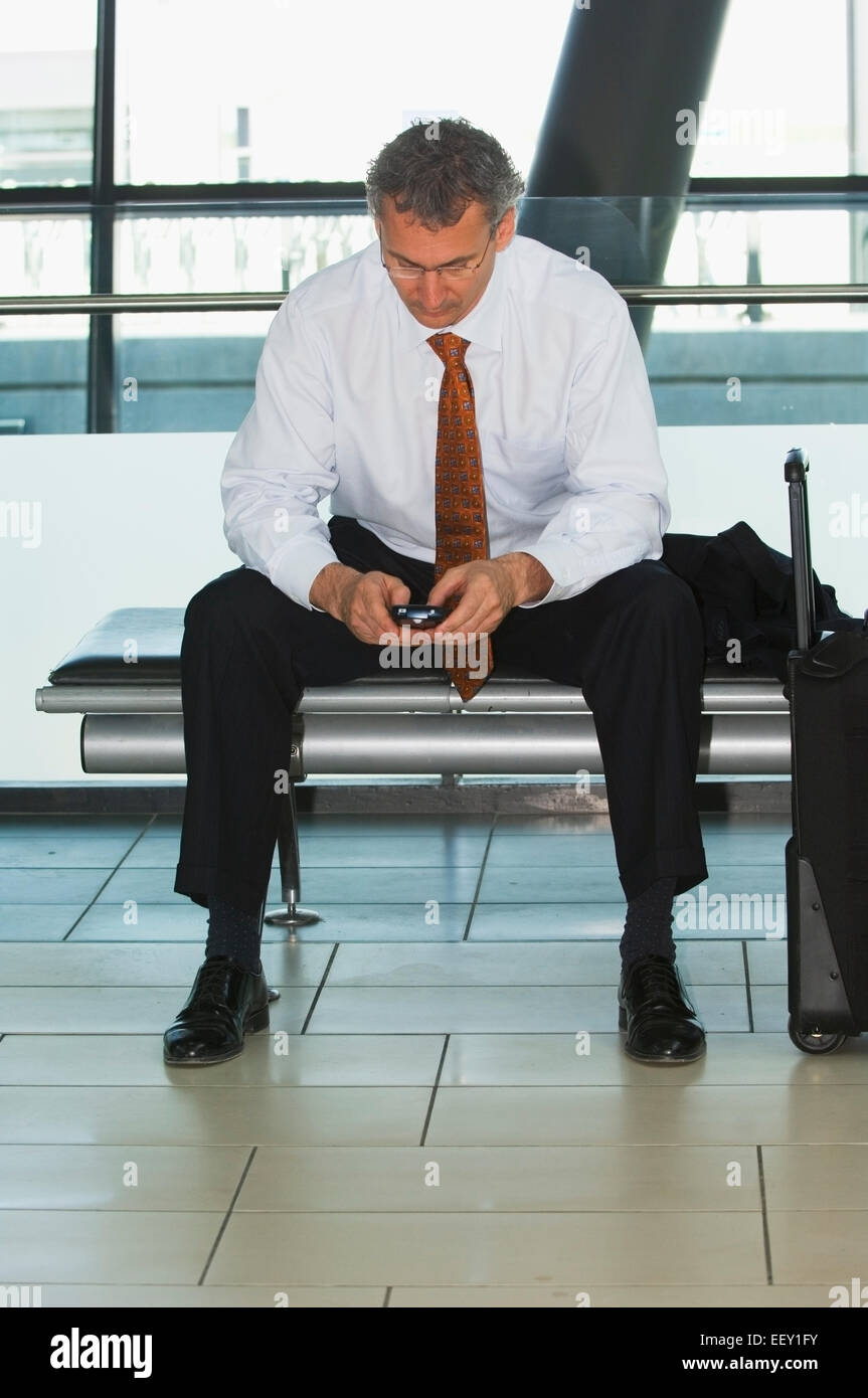 Businessman in airport using personal digital assistant Stock Photo